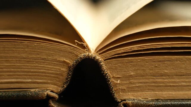 Close up of an old book with yellowed pages and a weathered binding turning