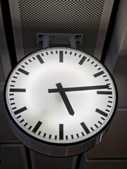 Large glowing round minimalist analog station clock at a modern transit platform, vertical view, symbolizing punctuality, travel schedules, and public transportation infrastructure.