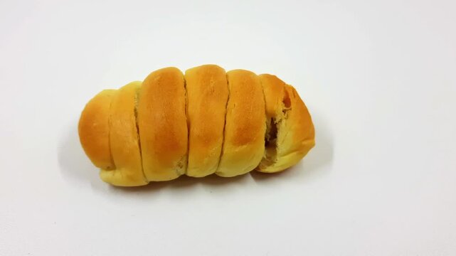 Golden baked sausage roll pastry sits isolated against a stark white background emphasizing its segmented shape and appealing golden brown color.