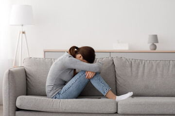Unhappy caucasian millennial woman suffering from depression and loneliness, sitting on sofa at...