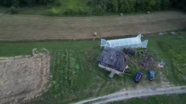 Aerial video of traditional Romanian wooden houses and a greenhouse in Glod village, Alba County, Romania, at golden sunset on August 15, 2025, with rolling hills and mountain horizon.