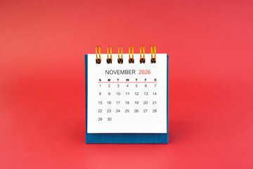 November 2026 white desk calendar on red background.
