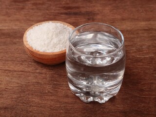 Salt water solution in glass with salt on wooden bowl on rustic wooden table. Concept for dietary supplements, health drinks, and daily nutrition	