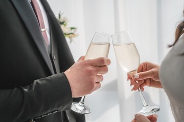 Caucasian middle aged man and Caucasian middle aged woman clinking champagne glasses during celebration, both hands visible holding drinks in bright indoor setting