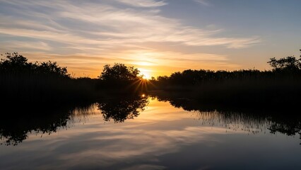 Obraz premium Peaceful golden hour sunset over a tranquil river, warm light reflecting on calm water, creating beautiful tree silhouettes against the vibrant twilight sky