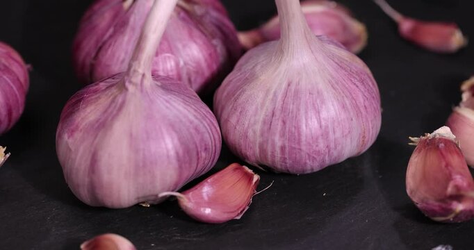 ripe purple garlic scattered on a black table in the kitchen and cloves of crushed garlic , garlic spices lie on a black board in the kitchen over cooking