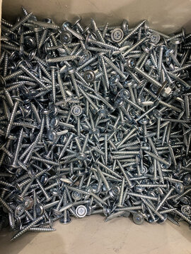 Large pile of silver metal screws with phillips heads in cardboard box, close-up. Fastener for construction or repair.