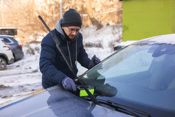 A guy is clearing snow from a car.