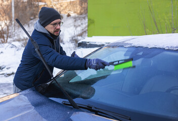 A guy is clearing snow from a car.