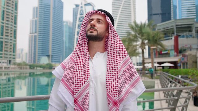 An Arab businessman stands alone in a modern urban area, displaying confidence and hope for future success in real estate business.