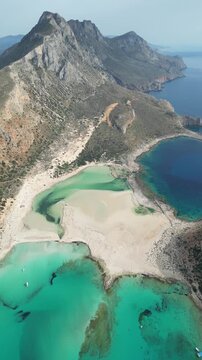 Greek coastal lagoon from above. Vertical 4K aerial video, Balos Bay in Crete, stunning nature, bright turquoise water, sandy beaches, unique meeting of three seas in a pristine Mediterranean location