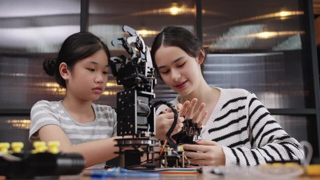 Asian and Caucasian young girls learning robotics together while building a robot arm in class.