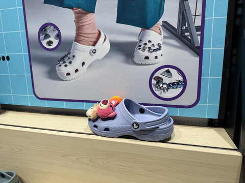 Lavender foam clog shoes with colorful plush animal jibbitz charms displayed on wooden shelf with retail product display screen background, Vietnam, Cam Ranh, January 17, 2026