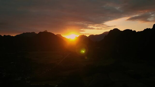 Paraglider flying above dramatic mountain landscape during golden hour at sunset. Scenic aerial view with warm sunlight creating a cinematic and adventurous atmosphere