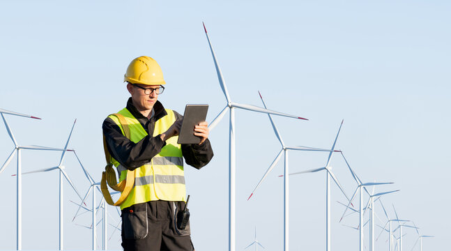Engineer with digital tablet works on a field of wind turbines