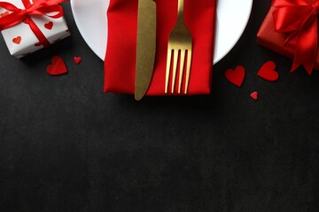 Valentine's Day concept. Top view photo with plate, cutlery, gift box, red hearts on black...
