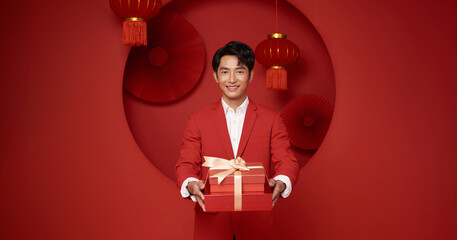 Chinese New Year gift giving concept Asian man holding elegant wrapped present in red festive studio expressing prosperity gratitude premium holiday gifting cultural tradition and celebration.