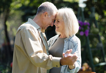 Tender aged spouses dancing in garden on spring day, touching foreheads and smiling, resting...