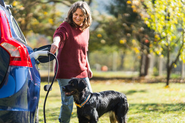 Woman with her dog next to charging electric car
