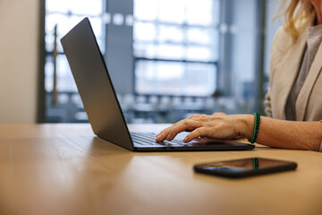 Woman manager typing on laptop at office desk, smart phone within reach. Workplace at corporate...