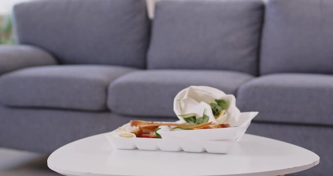 Junk food leftovers as cause of poisoning, stomach indigestion and nausea, unhealthy diet at home. Foam container lying on coffee table with spoiled takeaway fast food eaten for lunch or dinner