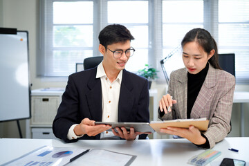 businesswoman and businessman analyzing financial charts and discussing business strategy at desk, both holding pens and reviewing printed documents together