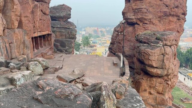 A breathtaking view of Badami city from the caves, framed between two massive red sandstone hills, highlighting the city&rsquo;s dense settlement and the scenic landscape of this historic Chalukyan site