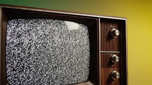 Nostalgic close-up view of a vintage wooden television set with three silver knobs against a bright yellow wall, displaying a static-filled screen that evokes retro charm and bygone technology