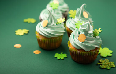 St. Patrick's Day vanilla and chocolate cupcakes with green frosting and  shiny clover decorations on green paper background. Irish holiday dessert concept, copy space.