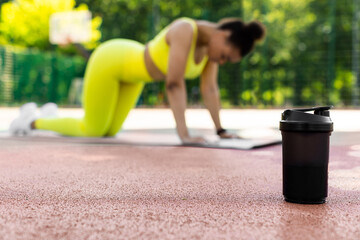 Sports Nutrition. Selective focus on black shaker on basketball field ground. Young black woman...