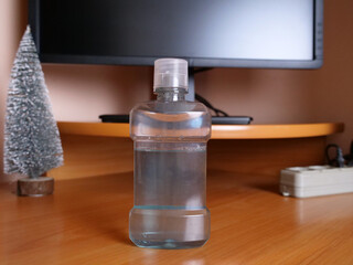 Clear plastic bottle with liquid standing on wooden desk in front of computer monitor.