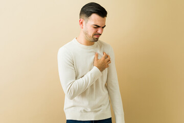 Latin man clutching chest with painful expression, experiencing sudden heart attack symptoms or anxiety
