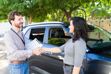 Professional driving instructor shaking hands with smiling adult woman near car, discussing successful driving lessons or new course