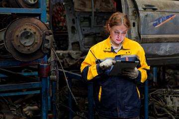 Worker working on a digital tablet in a garage full of vehicle parts