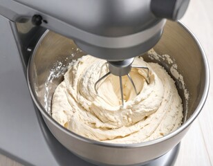 Close Up Of Silver Stand Mixer Whisking Light Beige Batter In Metal Bowl With Natural Lighting Illuminating Food Preparation In Kitchen Setting