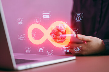 Hands hold a smartphone near a laptop with digital icons showing technology and finance concepts in a modern office