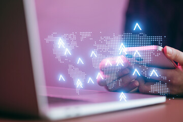 Person holding mobile phone with laptop nearby and digital world map on screen during a work project in a modern office setting