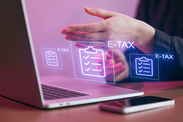 Hand gestures illustrate e-tax process while working on laptop at desk with smartphone nearby