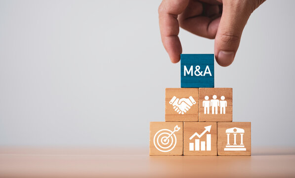 Hand placing M and A block on business strategy stack for mergers and acquisitions concept by represent corporate growth with partnership, investment strategy and financial performance.