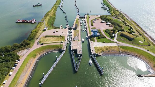 numerous white sailboats navigate through concrete passageways within complex system locks channels calm sun drenched waters sit between grassy embankments afsluitdijk netherlands lock 