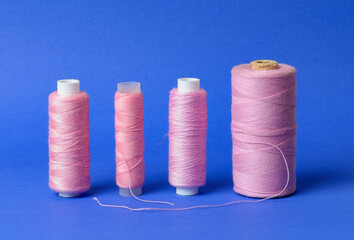 Spools with pink thread on blue background, orderly aligned in a row