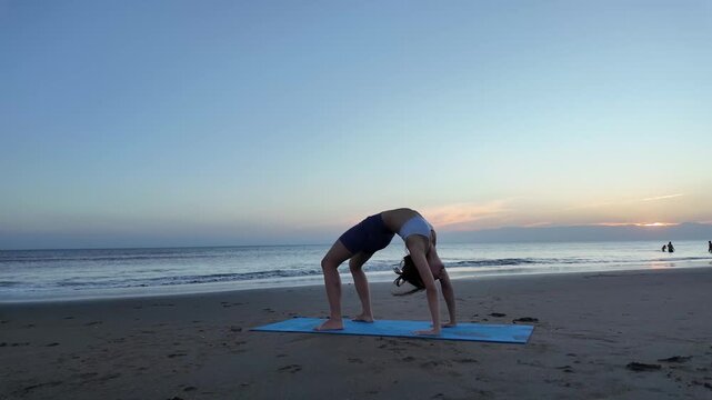 Lesbian woman practicing wheel pose yoga at sunset beach