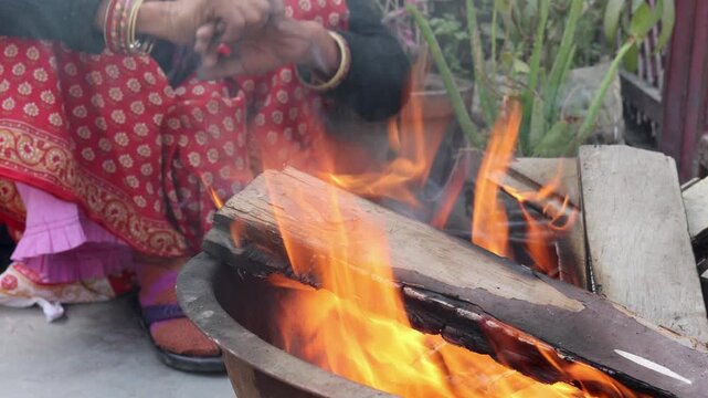 An Indian village woman warms her hands near an open fire, showing winter cold, traditional lifestyle, and everyday rural life practices in an Indian village setting.