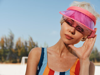 Bright portrait of a young woman wearing a pink visor and colorful striped swimsuit, sunlit face...