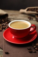 Fototapeta premium Cup with aromatic coffee, beans and napkin on wooden table, closeup