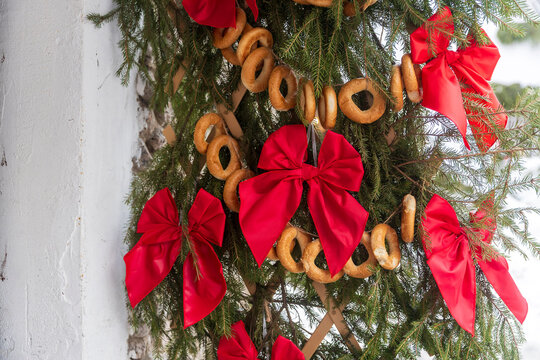 Traditional Slavic Christmas and New Year decorations featuring strings of drying sushki (bread rings) and vibrant red satin bows intertwined with natural green pine branches.