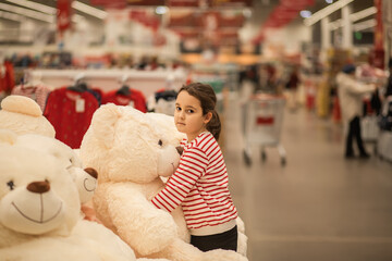 A young girl hugging a large white teddy bear in a store, wearing a red and white striped sweater,...