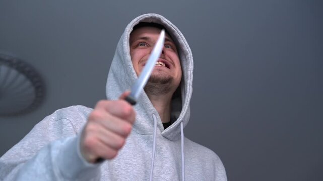 A hooded hooligan threatens someone with a knife.
The person attacks with a knife.
A sharp knife in the hands of an aggressive man.