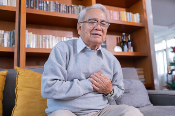 Elderly man grab his chest with hand suffer from chest pain in a living room