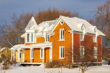 Beautiful red brick and clapboard siding Victorian style house with metal roof and turret seen during a partly sunny winter morning, St-Augustin-de-Desmaures, Quebec, Canada © Anne Richard